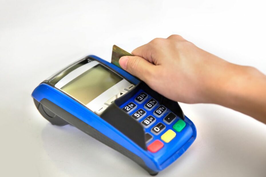 tangan sedang menggesek karu kredit atau debit di mesin EDC.