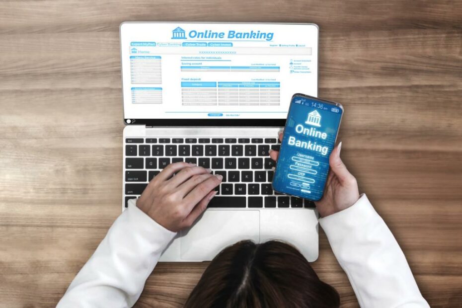 Seseorang sedang membuka aplikasi online banking di laptop dan handphone.