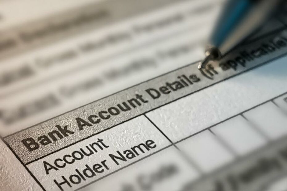 Kertas bertuliskan "Bank Account Details" dan "Account Holder Name" beserta pulpen di atasnya.