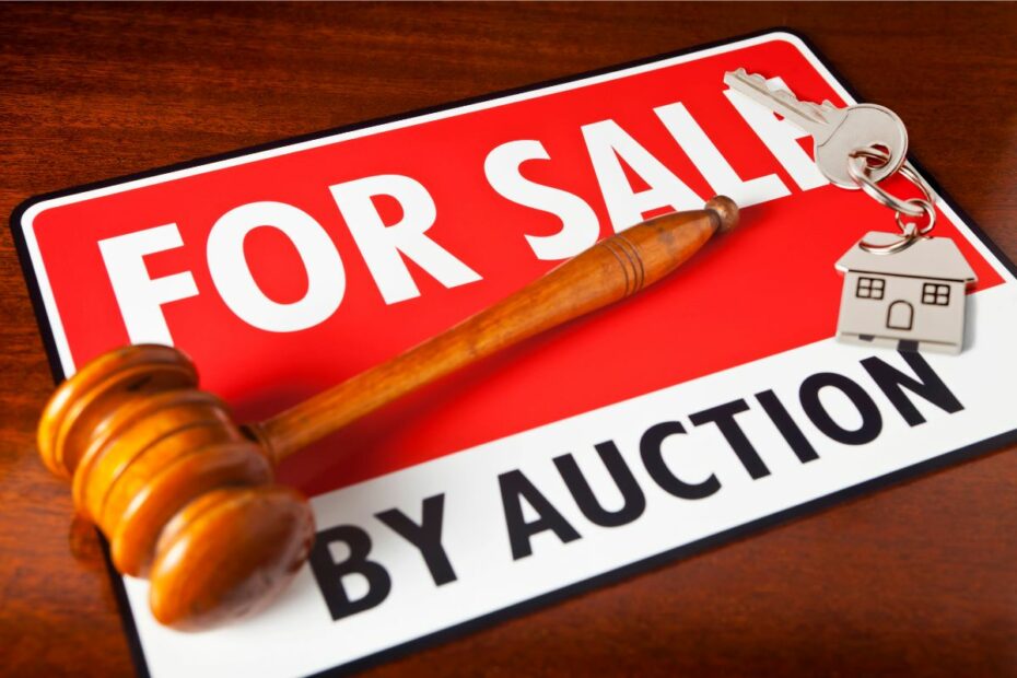 Papan bertuliskan "For Sale by Auction" dengan palu sidang dan kunci rumah di atasnya.