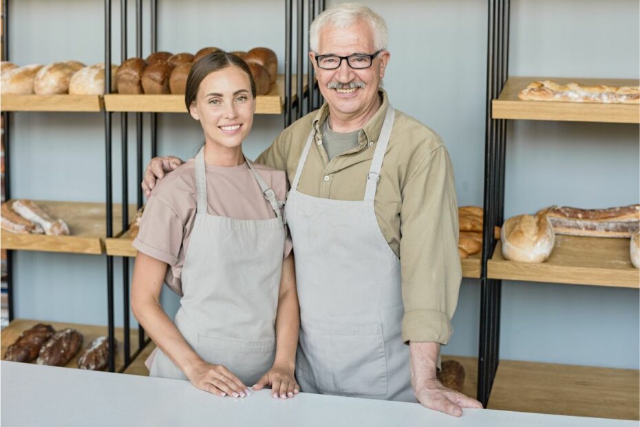 Seorang kakek sedang berdiri dengan wanita muda dengan latar rak berisikan roti yang merupakan bisnis keluarga.